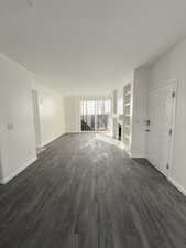 Unfurnished living room featuring dark hardwood / wood-style flooring and built in shelves