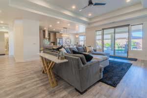 Living room with a raised ceiling, ceiling fan with notable chandelier, and light hardwood / wood-style flooring