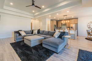 Living room featuring ceiling fan, a tray ceiling, sink, and light wood-type flooring