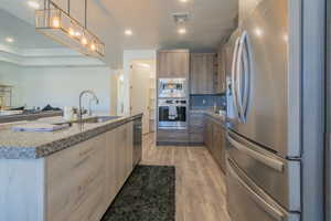 Kitchen featuring sink, hanging light fixtures, a center island with sink, light hardwood / wood-style flooring, and appliances with stainless steel finishes