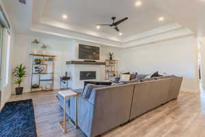 Living room with ceiling fan, light wood-type flooring, and a tray ceiling