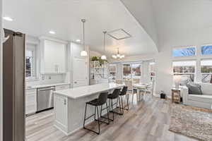 Kitchen with dishwasher, hanging light fixtures, a kitchen island, white cabinets, and a kitchen bar