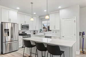 Kitchen with a kitchen island, appliances with stainless steel finishes, pendant lighting, white cabinets, and light stone countertops