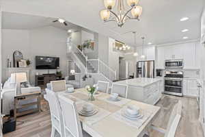 Dining room with ceiling fan with notable chandelier, vaulted ceiling, and light hardwood / wood-style floors