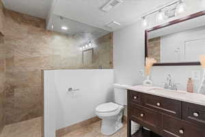 Bathroom featuring a tile shower, tile patterned flooring, vanity, toilet, and a textured ceiling