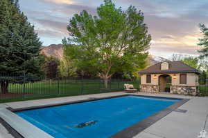 Pool at dusk with a yard, an outdoor structure, a mountain view, and a patio