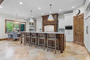 Kitchen featuring a large island, a breakfast bar, stainless steel microwave, white cabinets, and decorative light fixtures