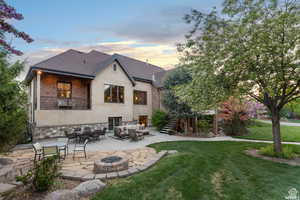 Back house at dusk featuring a balcony, a patio, a lawn, and an outdoor living space with a fire pit