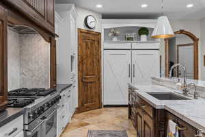 Kitchen featuring dark brown cabinetry, sink, light stone counters, hanging light fixtures, and double oven range