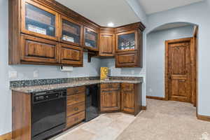 Kitchen featuring black dishwasher, sink, light colored carpet, and dark stone counters