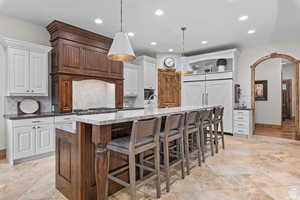 Kitchen featuring pendant lighting, white cabinets, a spacious island, and a kitchen bar