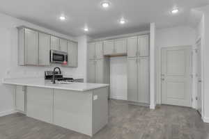 Kitchen featuring wood-type flooring, appliances with stainless steel finishes, gray cabinetry, and kitchen peninsula