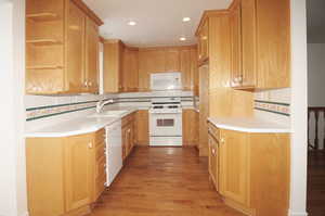 Kitchen with backsplash, white appliances, sink, and light wood-type flooring