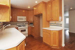 Kitchen with dark hardwood / wood-style floors, sink, backsplash, and white appliances