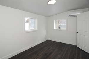 Empty room featuring an AC wall unit, a healthy amount of sunlight, dark wood-type flooring, and lofted ceiling