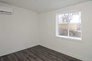 Unfurnished room with dark hardwood / wood-style flooring and an AC wall unit