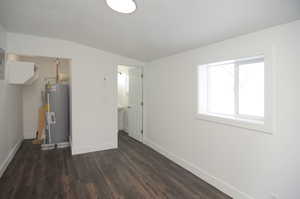 Unfurnished bedroom featuring dark hardwood / wood-style floors, vaulted ceiling, and water heater