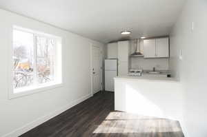 Kitchen with wall chimney exhaust hood, sink, white cabinetry, dark hardwood / wood-style flooring, and white fridge