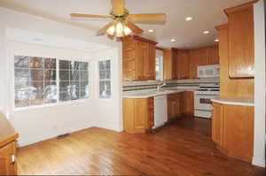 Kitchen featuring sink, decorative backsplash, ceiling fan, dark wood-type flooring, and white appliances