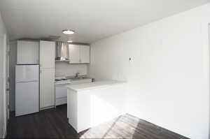 Kitchen featuring sink, white cabinetry, dark hardwood / wood-style flooring, white appliances, and wall chimney range hood