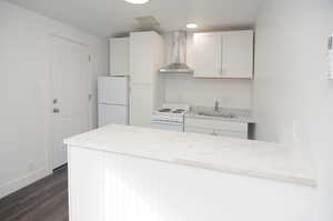 Kitchen with white cabinetry, sink, dark hardwood / wood-style flooring, white appliances, and wall chimney exhaust hood