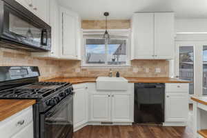 Kitchen with decorative light fixtures, butcher block counters, sink, and black appliances