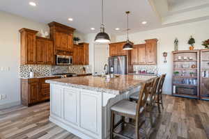 Kitchen with appliances with stainless steel finishes, pendant lighting, an island with sink, sink, and light stone counters