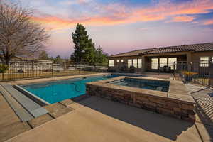 Pool at dusk featuring an in ground hot tub and a patio