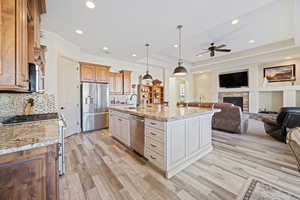 Kitchen with decorative light fixtures, appliances with stainless steel finishes, a raised ceiling, light stone countertops, and a kitchen island with sink