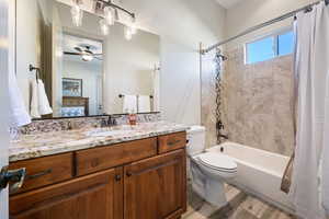 Full bathroom featuring hardwood / wood-style flooring, ceiling fan, vanity, shower / bath combination with curtain, and toilet