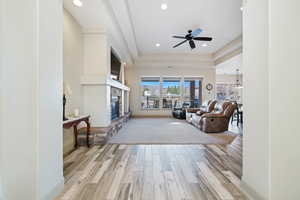 Living room with a stone fireplace, ceiling fan with notable chandelier, light hardwood / wood-style floors, and a tray ceiling