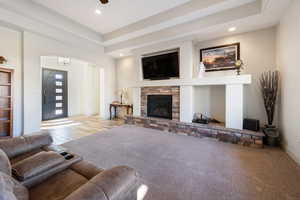 Living room with a fireplace, a raised ceiling, and ceiling fan