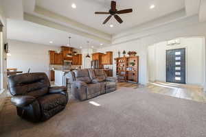 Living room featuring a tray ceiling, ceiling fan with notable chandelier, and light wood-type flooring