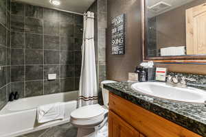 Full bathroom with a textured wall, toilet, vanity, visible vents, and shower / tub combo with curtain