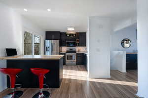 Kitchen featuring appliances with stainless steel finishes, a breakfast bar, kitchen peninsula, and light hardwood / wood-style flooring