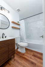 Full bathroom with hardwood / wood-style flooring, shower / tub combo, vanity, a textured ceiling, and toilet