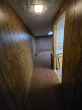 Hall with wood walls, a textured ceiling, and brick wall