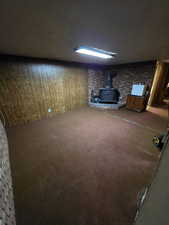 Basement with carpet floors, brick wall, a wood stove, and a textured ceiling