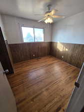 Unfurnished room featuring wooden walls, dark hardwood / wood-style floors, and ceiling fan