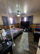 Bedroom featuring dark hardwood / wood-style floors, ceiling fan, and wood walls