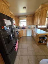 Kitchen featuring sink, black fridge, light tile patterned floors, white dishwasher, and backsplash