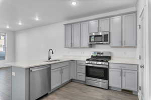 Kitchen with appliances with stainless steel finishes, kitchen peninsula, sink, and hardwood / wood-style floors