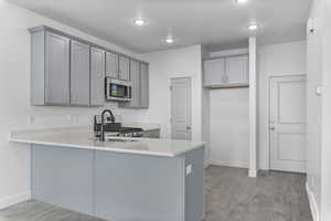 Kitchen with gray cabinetry, light hardwood / wood-style floors, kitchen peninsula, and appliances with stainless steel finishes