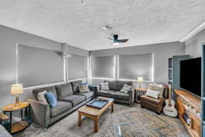 Carpeted living room with ceiling fan and a textured ceiling