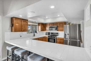 Kitchen featuring a kitchen bar, sink, tile countertops, appliances with stainless steel finishes, and kitchen peninsula