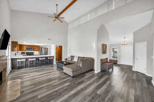 Living room with dark wood-type flooring, high vaulted ceiling, and ceiling fan with notable chandelier