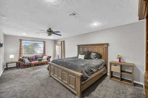 Bedroom with ceiling fan, a textured ceiling, and dark colored carpet