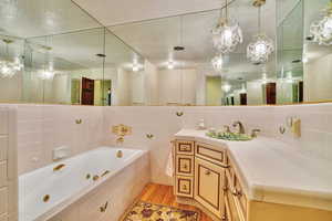 Bathroom with tile walls, hardwood / wood-style floors, vanity, tiled bath, and a textured ceiling