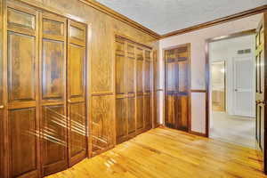 Corridor with crown molding, light hardwood / wood-style flooring, and a textured ceiling