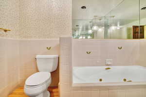 Bathroom featuring a relaxing tiled tub, wood-type flooring, toilet, and tile walls